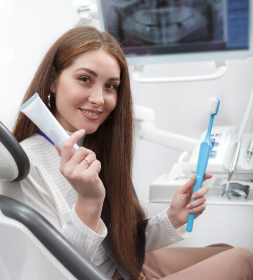 Vertical portrait of a cheerful woman holding toothbrush and toothpaste, sitting in dental chair